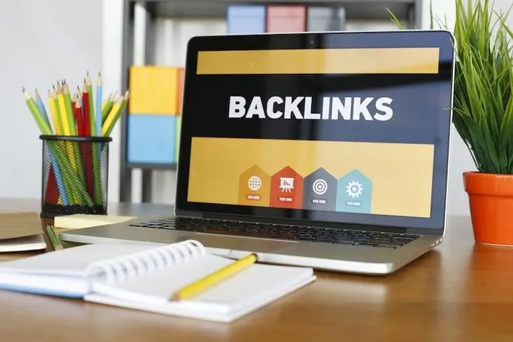 حاسوب محمول يعرض كلمة BACKLINKS على مكتب به دفتر ونبتة